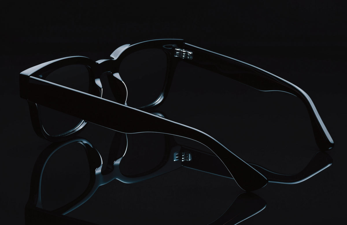 Heavy black acetate sunglasses on a black surface under hard studio light