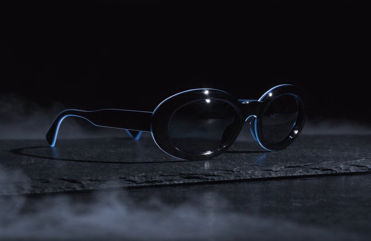 Black acetate sunglasses with a cold blue rim light on dark slate