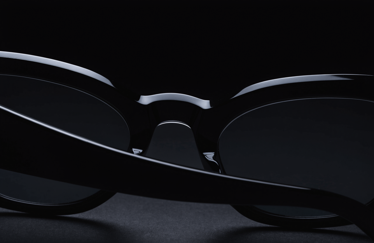 Black acetate sunglasses with smoke lenses on a black surface under a single hard light, illustrating the best luxury sunglasses under $200