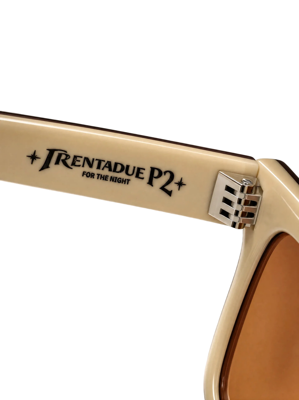 Close-up of a cream-colored sunglasses arm with black printed text reading 'TRENTADUE P2 FOR THE NIGHT' and a silver hinge, against a neutral gray background.
